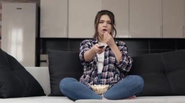 Karantina sırasında mutfakta genç bir kadın. Bacak bacak üstüne atmış bir şekilde kanepeye otur ve televizyon ya da film izle. Sıkıcı kız televizyon kanallarını değiştiriyor. İyi bir film arıyorum. Patlamış mısır yemek..