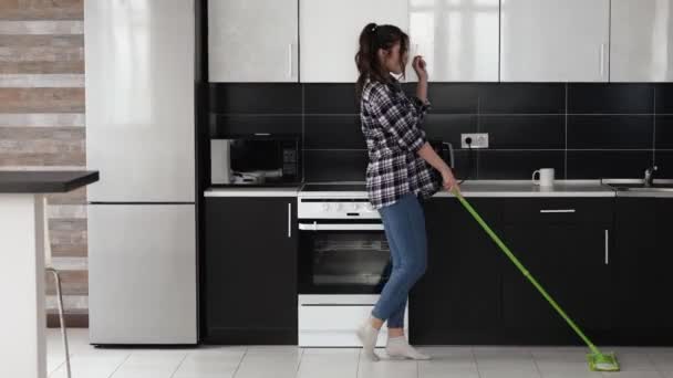 Mujer joven en la cocina durante la cuarentena. Bailando y limpiando piso con fregona. Casa esposa disfrutando de tiempo en la cocina . — Vídeos de Stock