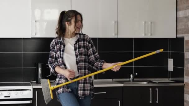 Young woman in kitchen during quarantine. Stand alone and pretend to play on mos as on guitar. Have fun, dancing and singing out loud during cleaning. Slow motion. — Stock Video