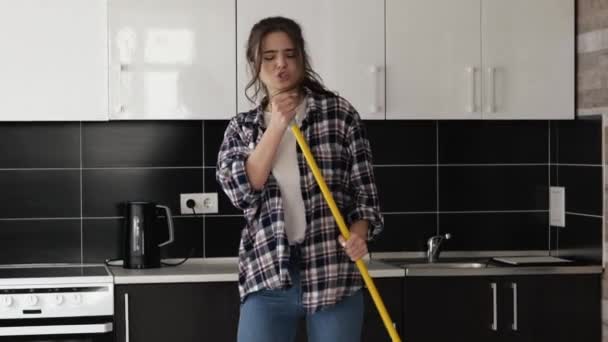 Young woman in kitchen during quarantine. Girl hold mop in hands and singing. Pretent holding microphone and dance alone in apartment. Have fun in slow motion. — Stock Video