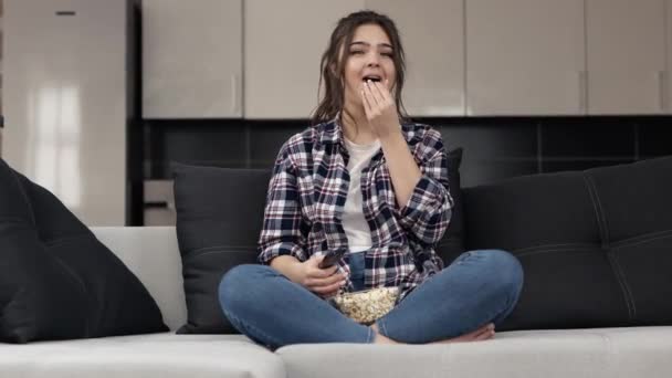 Giovane donna in cucina durante la quarantena. Siediti sul divano e guarda la TV o il film. Scambio canali televisivi e mangio popcorn. Ridere e divertirsi . — Video Stock