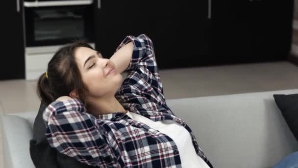 Young woman in kitchen during quarantine. Sit down on sofa and rest. Hold arms crossed behind head. Enjoy rest with pleasure. Slow motion. — Stock Video