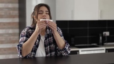 Karantina sırasında mutfakta genç bir kadın. Hasta, beyaz dokuya hapşırıyor. Alerji ya da hastalıktan muzdarip. Videodaki hasta kadın..