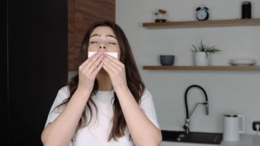 Karantina sırasında mutfakta genç bir kadın. Baş ağrısı ve burun akışı. Beyaz dokuya hapşırıyor. Kız acıdan muzdarip. Hasta ve hasta bir kadın..