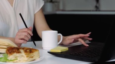 Karantina sırasında mutfakta genç bir kadın. Bilgisayarla internette arama yaparak uzaktan kumandada çalışan bir kızın görüntüsünü kes. Verimli iş.