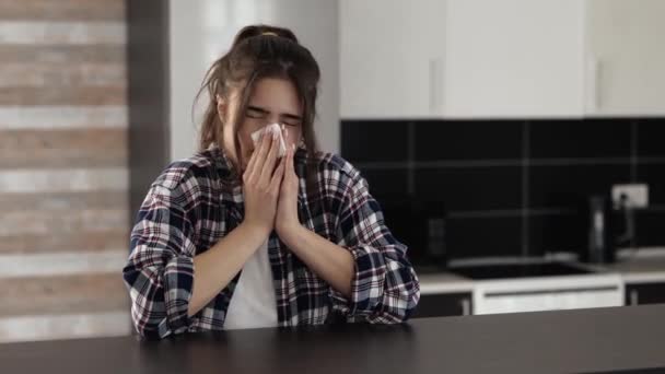 Jonge vrouw in de keuken tijdens quarantaine. Meisje zit aan tafel en niest. Lijden aan neus lopen en ziekte. Ill vrouwelijke persoon alleen in appartement. — Stockvideo