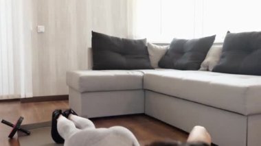 Genç bir kadın karantina sırasında evde egzersiz yapıyor. Haltersiz yoga minderinde şınav çekmek. Apartmanda aktif ince model egzersizi. Kamera geri gidiyor.