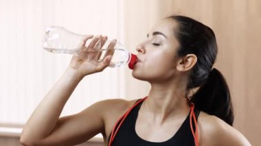 Genç bir kadın karantina sırasında evde egzersiz yapıyor. Tek başına dur ve egzersizden sonra su iç. Reklamlar. Susuzluk zamanı..