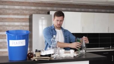 Karantina sırasında mutfakta genç bir adam. Plastik şişeyi diğer çöplerden ayırıp mavi kovaya koyuyorum. Sorumlu kullanım. Çevreye dikkat et. Sıfır atık.