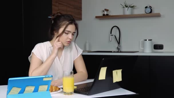 Karantina sırasında mutfakta genç bir kadın. Evde çalışan mutsuz bir kız. Laptop ve tablet kullanarak. Ağladığın için ellerinle yüzünü ört.. — Stok video