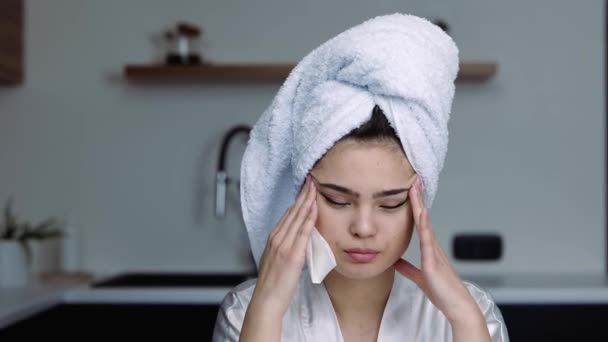 Młoda kobieta w kuchni podczas kwarantanny. Dziewczyna w kąpieli ubrania cierpią z powodu bólu głowy lub bólu. Chora kobieta masująca jej głowę. Grypa lub choroba. — Wideo stockowe