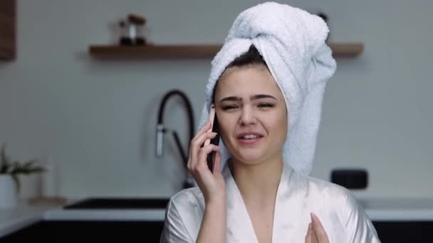 Młoda kobieta w kuchni podczas kwarantanny. Dziewczyna rozmawia przez telefon i się kłóci. Kobieta rozmawia na głos. Kobieta model po prysznicu w białej kąpieli ubrania. — Wideo stockowe