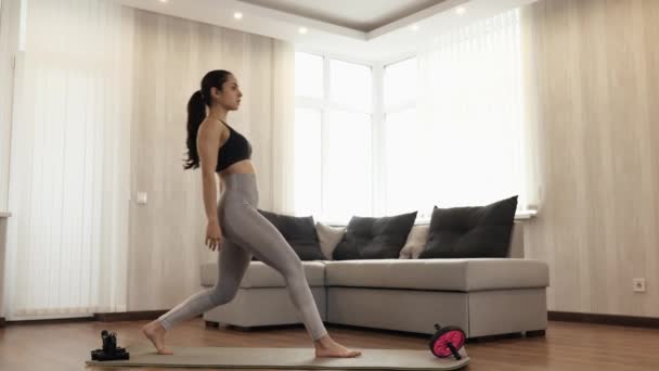 Ung kvinna har träning hemma under karantänen. Stå rakt på yogamattan och inta ett ben trupp eller krigare asana position. Lugn och koncentrerad. — Stockvideo