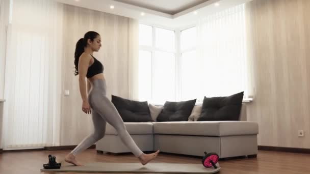 Genç bir kadın karantina sırasında evde egzersiz yapıyor. İnce yapılı bir model yoga pozisyonunda tek bacaklı bir reklamcıyla çömelme egzersizi yapıyor. Göğüs bölgesinde el ele tutuşun. Sakin ve kendinden emin. — Stok video