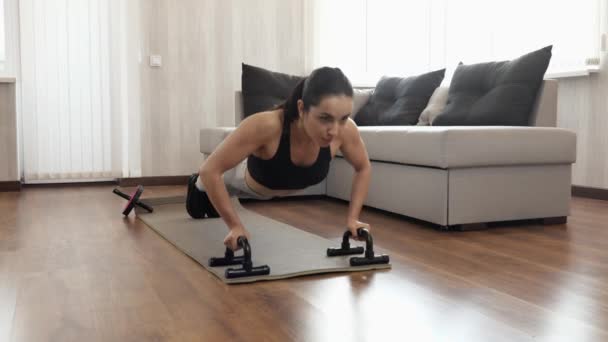 Jonge vrouw heeft thuis training tijdens quarantaine. Voorvoew van sterke krachtige vrouwelijke persoon doen push-ups met sportuitrusting. Camera verplaatsen naar vrouw blijven oefenen. — Stockvideo