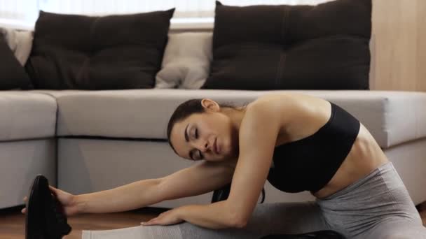 Young woman has workout at home during quarantine. Slim model stretching back down to her legs and toes on feet. Warming up before exercising. Camera moves back in slow motion. — Stock Video