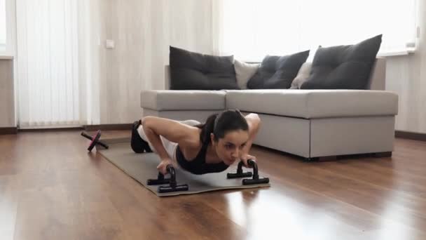 Jonge vrouw heeft thuis training tijdens quarantaine. Actieve push-ups met halters op yoga mat. Wapens sterker maken. — Stockvideo