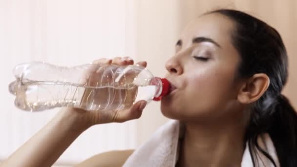 Während der Quarantäne trainiert die junge Frau zu Hause. Beginnen Sie, Wasser aus der Flasche zu trinken. Aqua-Werbung. Wasser trinken nach hartem Training. — Stockvideo