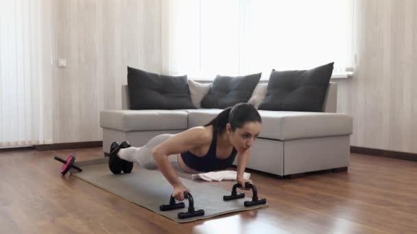 Una mujer joven hace ejercicio en casa durante la cuarentena. Haciendo flexiones con pesas. Entrenamiento solo con intenso. Manos y cuerpo fuertes . — Vídeos de Stock