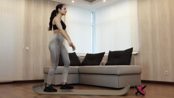 Jonge vrouw heeft thuis training tijdens quarantaine. Slim fit vrouwelijk model doet een been squat oefening. Stap naar voren en stap achteruit.. — Stockvideo