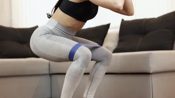 Mladá žena má doma během karantény cvičení. Nízký pohled na výkonný štíhlý model dělá squat cvičení se sportovní žvýkačkou. Zpomalený pohyb. — Stock video