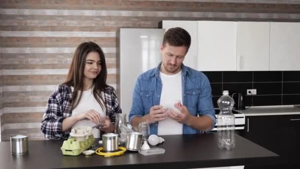 Young couple in kitchen during quarantine. Man and woman sorting trash and prepare it for recycling. Responsible people for saving environment. — Stock Video
