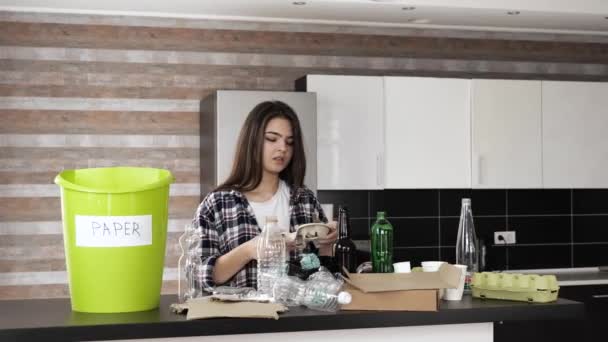 Mujer joven en la cocina durante la cuarentena. Chica clasificando papel de otra basura y hacia fuera en cubo verde. Cero desperdicio estilo de vida. Uso responsable. Cuida el medio ambiente . — Vídeo de stock