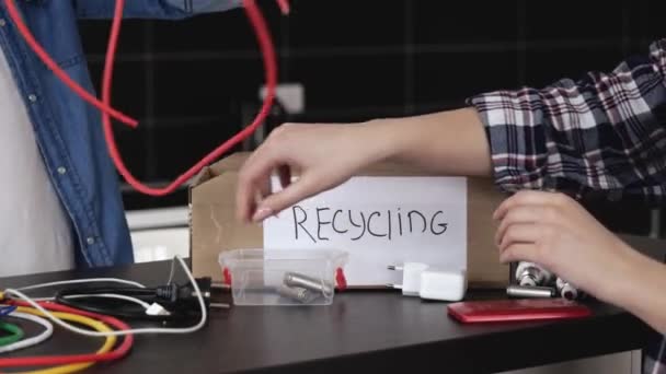 Pareja joven en la cocina durante la cuarentena. Cierre de la caja de reciclaje para cables eléctricos y cables. Hombre y woamn fuera también bombillas en él . — Vídeos de Stock