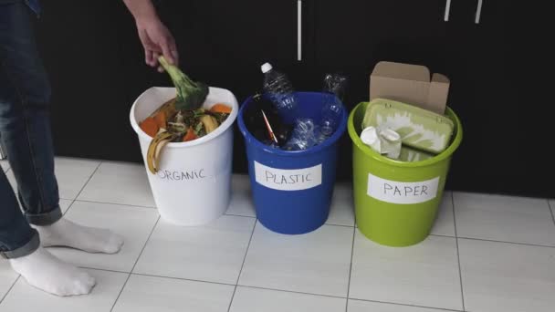 Un joven en la cocina durante la cuarentena. Tres cubos en el suelo para residuos orgánicos, de papel y plásticos. Lanzamiento de brócoli en cubo de residuos orgánicos y poner allí la piel de plátano . — Vídeo de stock
