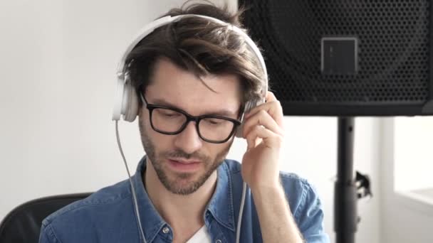 Молодий чоловік у студії звукозапису. Повільний рух хлопця, який слухає музику через навушники. самотужки в кімнаті і насолоджуватися нею . — стокове відео