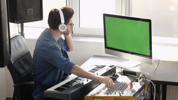 Giovanotto in studio di registrazione del suono. Siediti da solo e utilizza la console di mixaggio musicale con il computer. Schermo verde digitale. Registrazione del suono in camera . — Video Stock