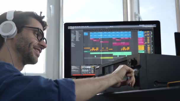 Jongeman in geluidsopnamestudio. Guy in slow motion verandert muziekvolume met rechterhand op speciale console. Liedjes beluisteren via een hoofdtelefoon. — Stockvideo