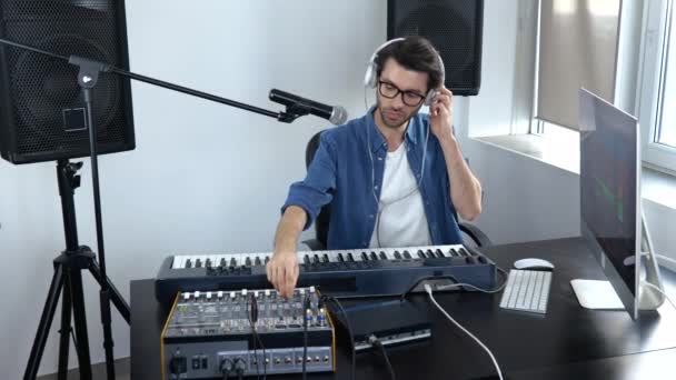 Jovem no estúdio de gravação de som. Guy em câmera lenta ajustando o console de mixagem de música e ouvindo-o em fones de ouvido . — Vídeo de Stock