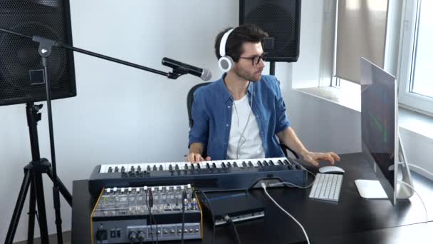 Jeune homme en studio d'enregistrement sonore. Mouvement lent de l'homme de son joyeux réglage de la console de musique. Étudiant apprenant à jouer au clavier . — Video