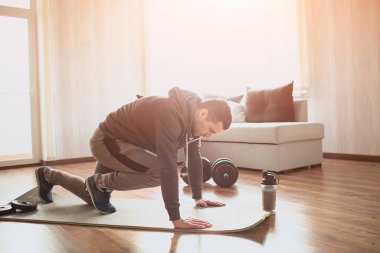 Genç, sıradan bir adam spor olsun diye evine gidiyor. Bacakları olan bir yerde koşarak karın kası egzersizi yapan sıradan bir adamın resmi. Birinci sınıfların vücut ısıtması. Güneşli bir dairede tek başına geriniyorsun..