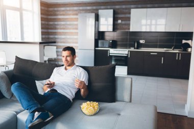 Genç adam kendi dairesinde televizyon izliyor. Kanepede tek başına otur ve abur cubur ye. Televizyon kanallarını değiştirmek için uzaktan kumanda kullan. İlginç film ya da program aranıyor.
