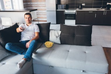 Genç adam kendi dairesinde televizyon izliyor. Neşeli, mutlu, çekici, sıradan bir adam. Uzaktan kumandayı düz elle tutuyor. Televizyon kanalı değiştiriliyor. Kendini evinde eğlendir..