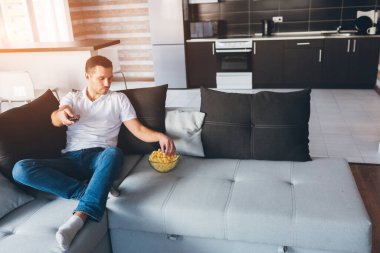 Genç adam kendi dairesinde televizyon izliyor. Ciddi konsantre adam elinde uzaktan kumandayla kaseden atıştırmalık bir şeyler alır. Odada tek başına film ya da televizyon izlersin. Sakin sakin sıradan bir adam..