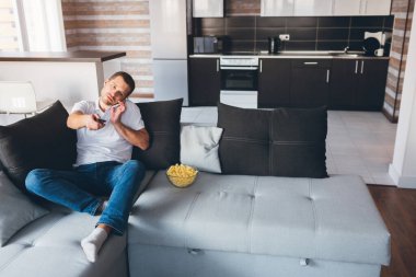 Genç adam kendi dairesinde televizyon izliyor. Aynı anda hem telefonla konuşup hem de uzaktan kumandayı kullanarak. Sinema kanalı değiştiriyor. Odada tek başına eğleniyorsun. Modern teknolojiler. Telefon..