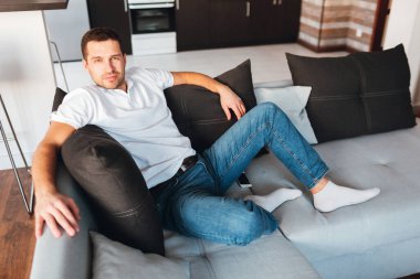 Genç adam kendi dairesinde televizyon izliyor. Kamerada poz verip gülümseyen neşeli, kendine güvenen bir adam. Rahat bir kanepeye otur ve poz ver. Odada tek başına. Biraz gülümse. Mutlu, neşeli adam..