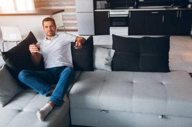 Genç adam kendi dairesinde televizyon izliyor. Adam kanepeye oturup elinde bir bardak alkolle televizyon izliyor. Mutlu pozitif genç adam viski ya da brendi içer. Rahatla ve dinlen..