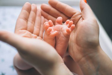 Yeni doğmuş bir bebeğin ayaklarına yakın çekim. Genç anne, pençelerinde bebek ayakları tutuyor. Küçük bebek çocuk masasında yatıyor. Pencerenin yanındaki bebek masasında yeni doğmuş bir çocuk var..