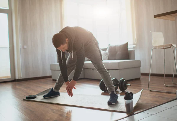 Young ordinary man go in for sport at home. Adult male person stretching down to his feet with hands. Warm up body before first training. Freshman and beginner in action. — Stock Photo, Image