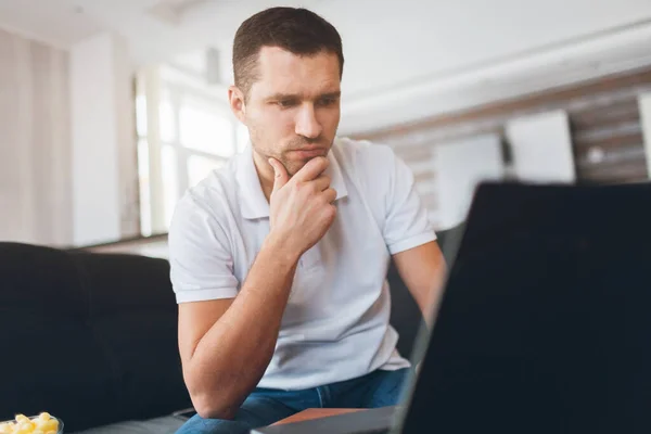 Young man watch tv in his own apartment. Concentrated confident guy watching sport match, game or program. Also watch movie or film. Intension looking at screen.