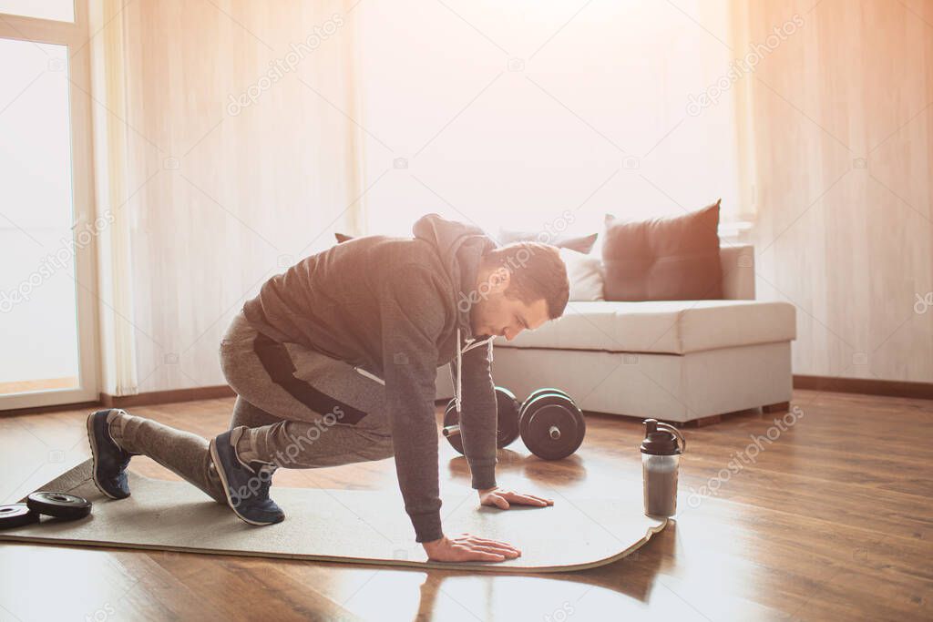 Young ordinary man go in for sport at home. Picture of real ordinary man doing abs exercising by running on one place with legs. Worksout freshman warming up body. Stretching alone in sunny apartment.