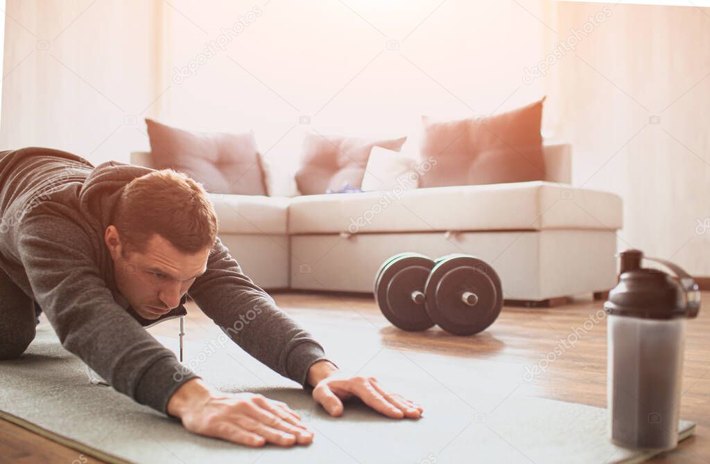 Young ordinary man go in for sport at home. Cut view of beginner guy stretching his body and pull hands foward on mat. Improving body shape. Real man with no knowledge in sport start workout.