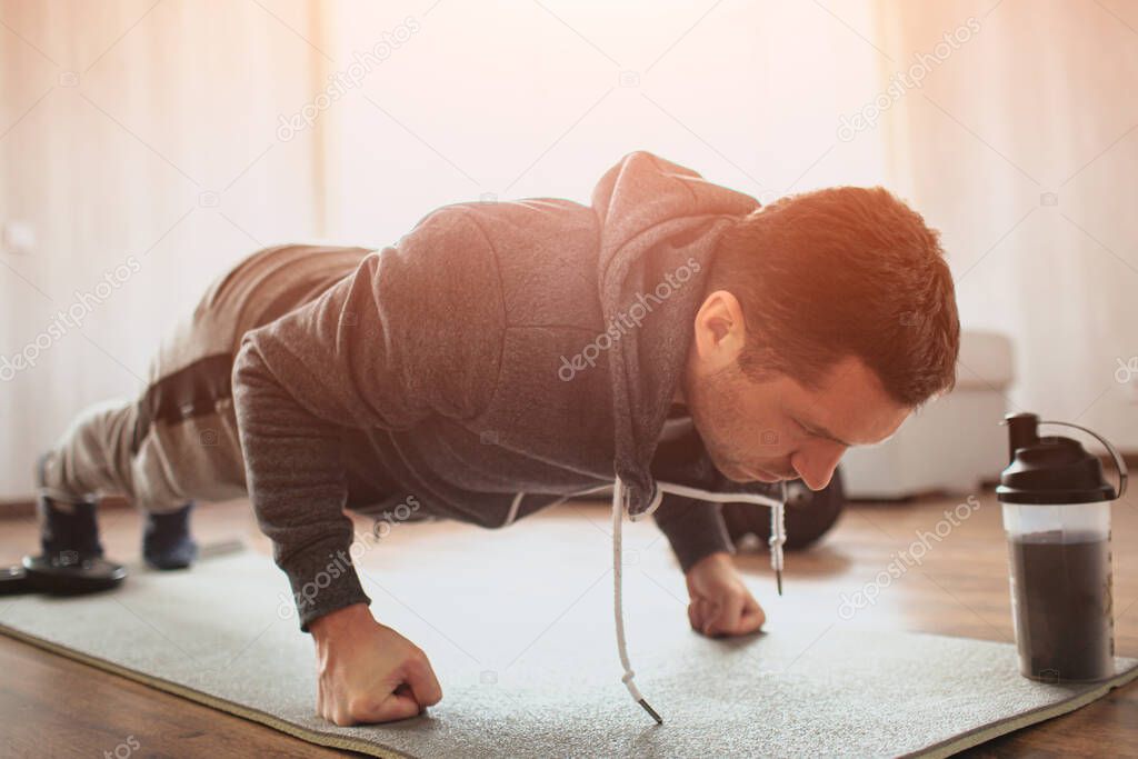 Young ordinary man go in for sport at home. Stand in plank position on his fists or doing push ups exercising. Hardworking beginner or ordinary man improving his body. Start workout without trainer.