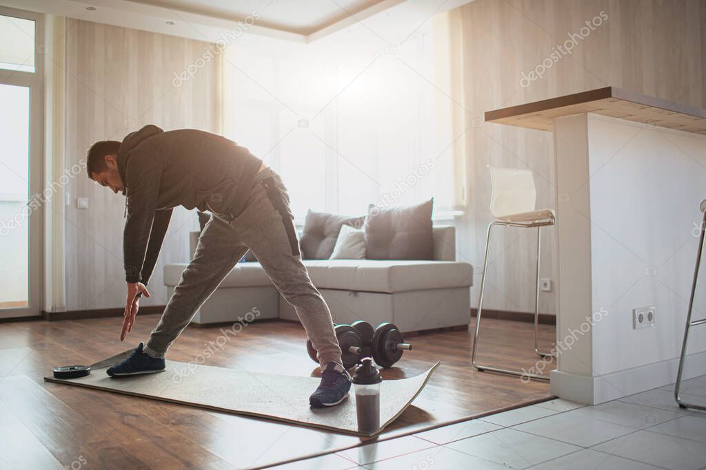 Young ordinary man go in for sport at home. Guy warking on his body shape to get better. Beginner in sport stretching his tie with both hands. Working out alone in apartment. Concentrated persisted.
