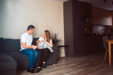 Anne ve baba yeni doğmuş bir bebekle oturma odasında. Yaşamın ilk yılı. Bakım ve sağlık. Annem kucağında küçük bir çocuk tutuyor ve babam onun yanında oturuyor..