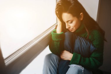 Mutsuz genç bir kadın pencerenin yanında üzgün. Esmer kadın ağlıyor. Üzüntü, ilgisizlik, depresyon ve melankoli..